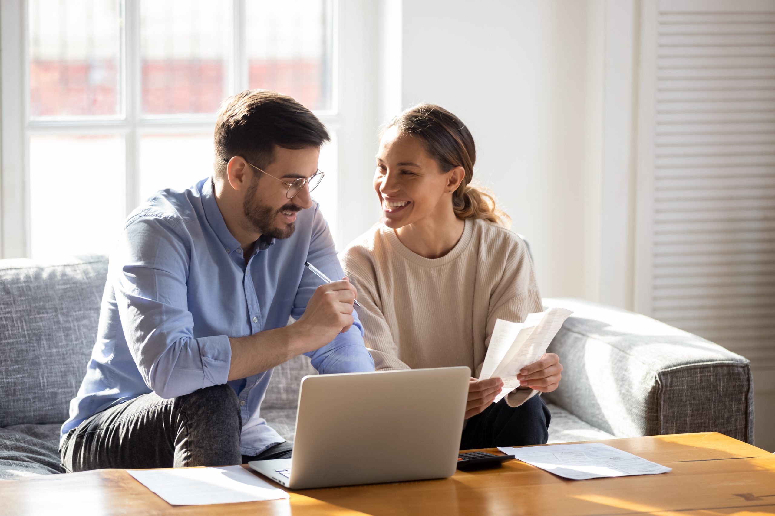 Happy,Young,Married,Couple,Sit,On,Couch,Calculate,Expenses,Use computer.jpg